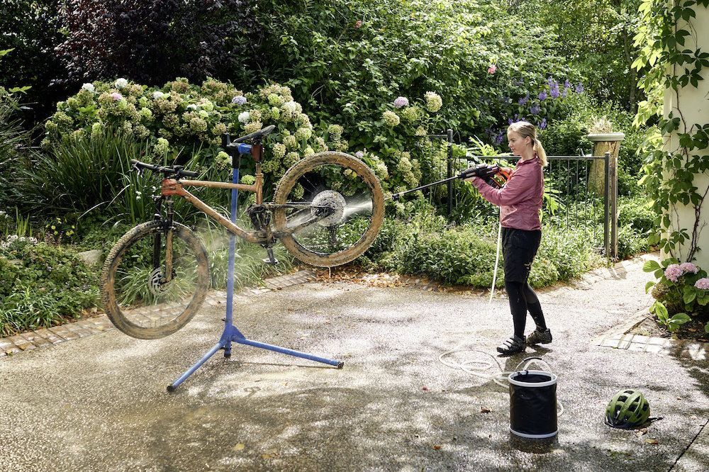 Person reinigt Fahrrad mit Hochdruckreiniger.